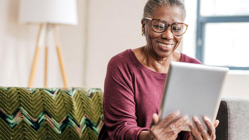 A woman sits on a sofa in her home and looks at an ipad.