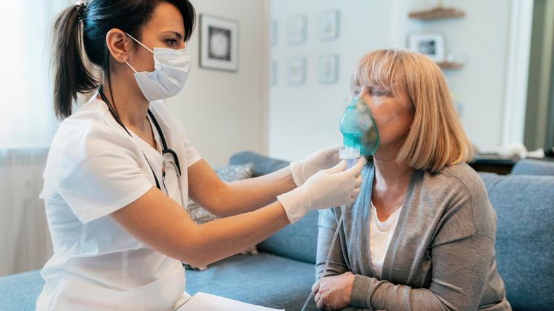 A respiratory therapist works with a female patient in her home.