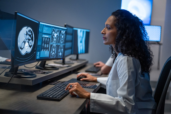 A female physician looks at a row of computer screens showing diagnostic radiology scans.