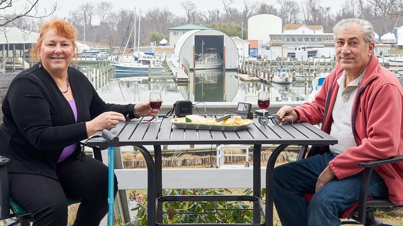 Lynne Jacobs and her husband Greg are pictured sharing a meal at an outdoor restaurant with a boat marina in the background..