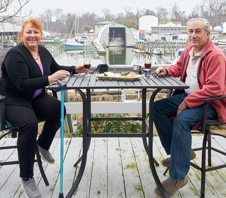Lynne Jacobs and her husband Greg are pictured sharing a meal at an outdoor restaurant with a boat marina in the background..