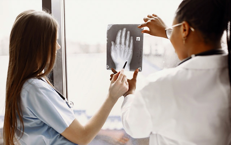 Two doctors examine an x-ray film of a patient's hand.