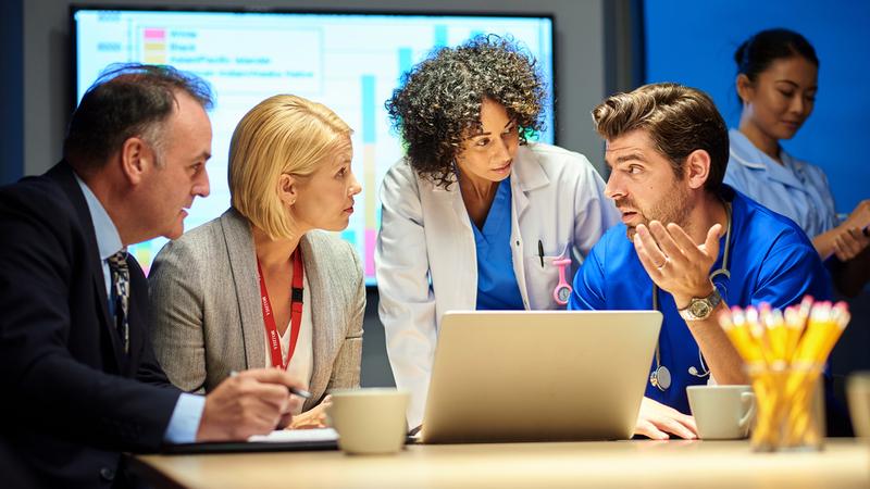 a mixed group of healthcare professional and business people meet around a conference table.