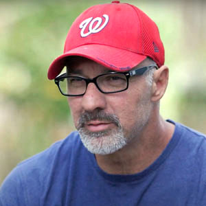图为一名戴着红色棒球帽的男子，他在COVID-19康复期间接受了远程患者监测。