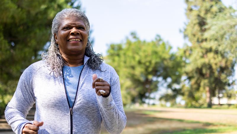 An African-American woman goes for a run in a park to maintain a healthy lifestyle.