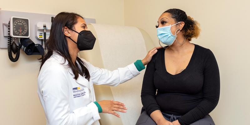 Dr Ahmareen Baten talks with a patient during an office visit at MedStar Health. Both people are wearing masks.