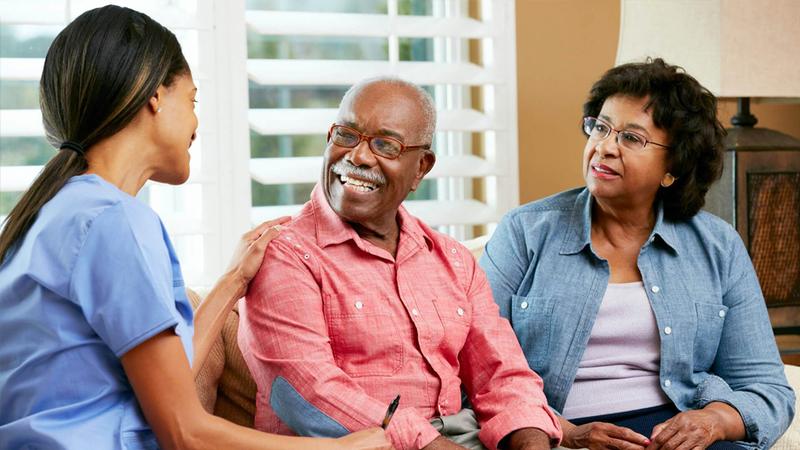 A nurse sits with a patient and his wife.