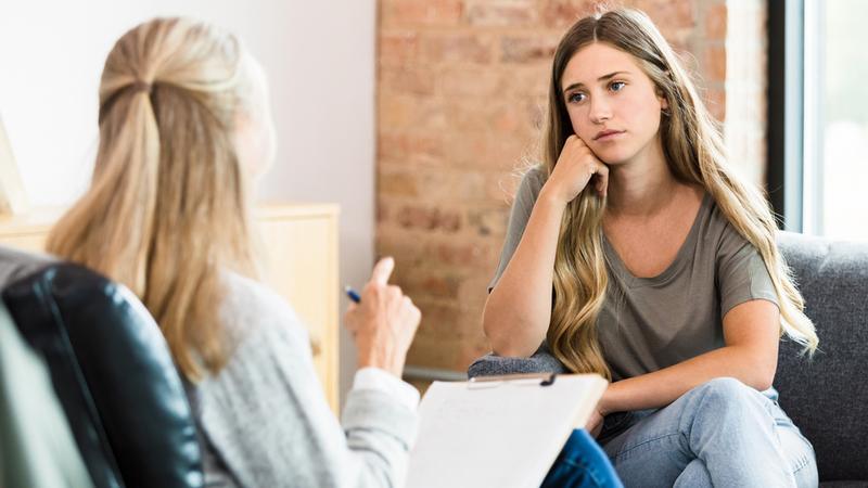 A young woman talks with a therapist in an office setting.
