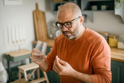 A man takes medicine in the kitchen of his home.