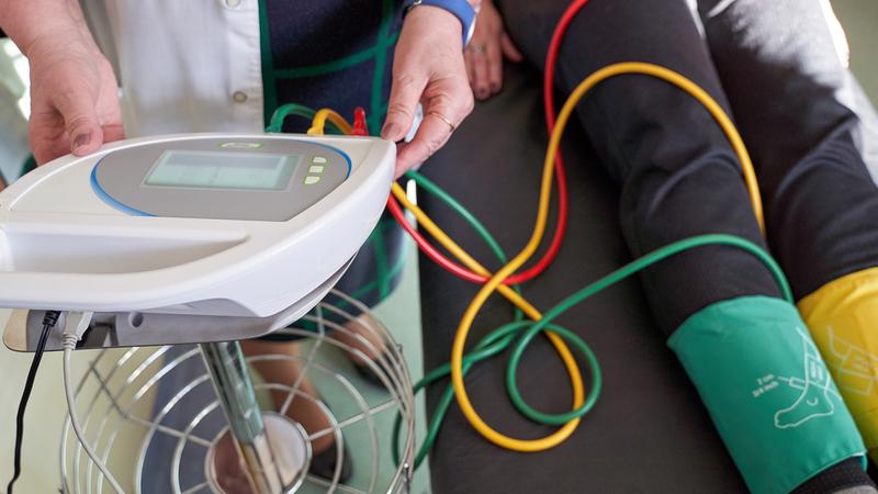 A doctor uses a monitor to check the blood pressure in a patient's ankle during a vascular test.