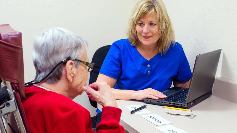A speech language specialist  treats communication skills of a senior aged woman in a clinic setting.