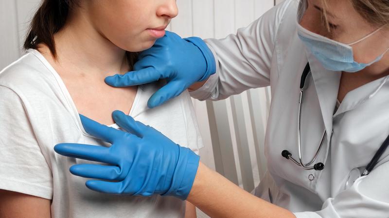 A dermatologist looks at the skin of a young patient during an office visit.