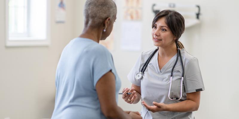 A female doctor talks with a female patient in a clinical setting.