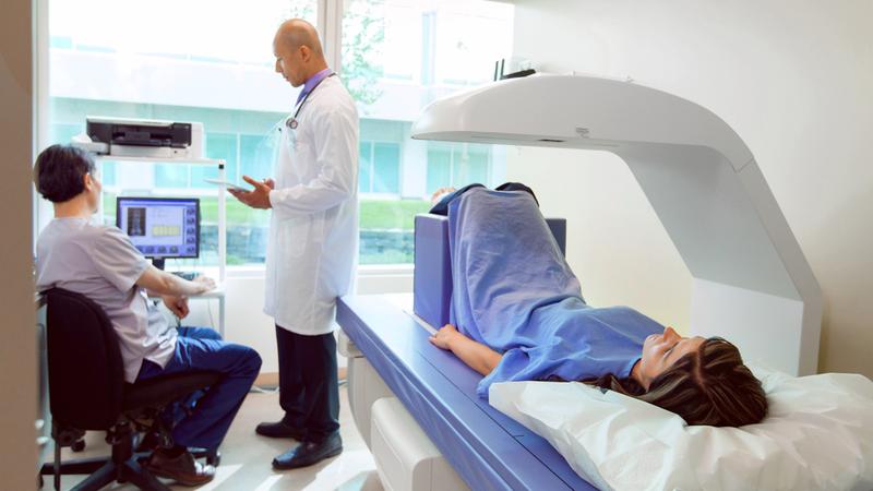 A patient undergoes a bone density scan while a doctor and a radiologist monitor the results.