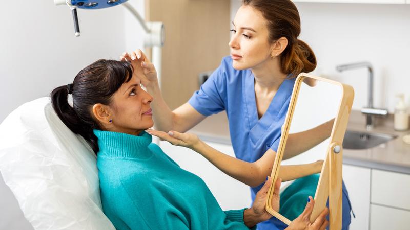 A dermatologist examines the face of a female patient in a clinical setting.