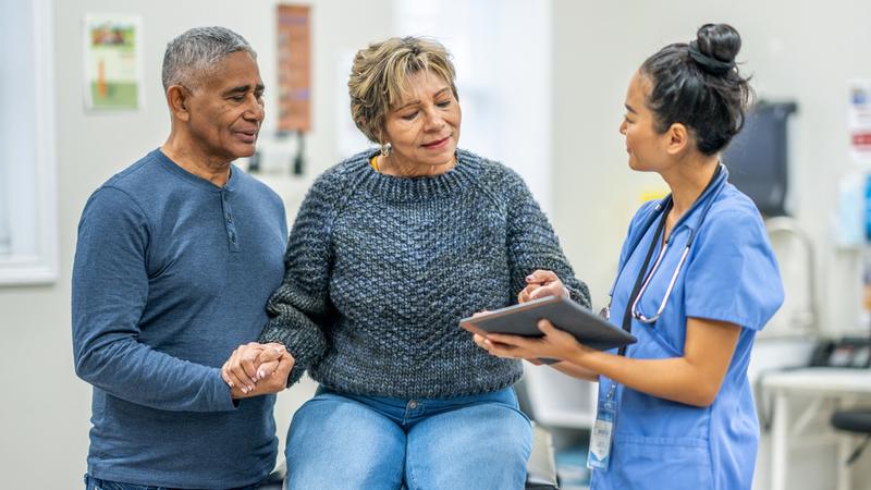 A nurse talks with a husband and wife in a clinical setting.