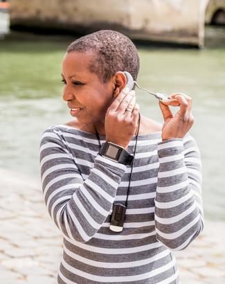 A young woman puts in her cochlear implant device while standing outdoors.