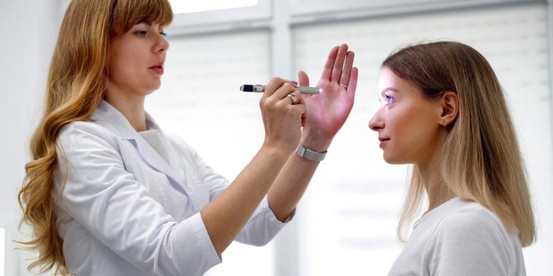 A doctor shines a light in the eyes of a female patient during an office visit.
