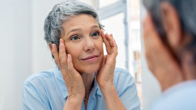 A mature adult woman looks closey at her eyes in a mirror.