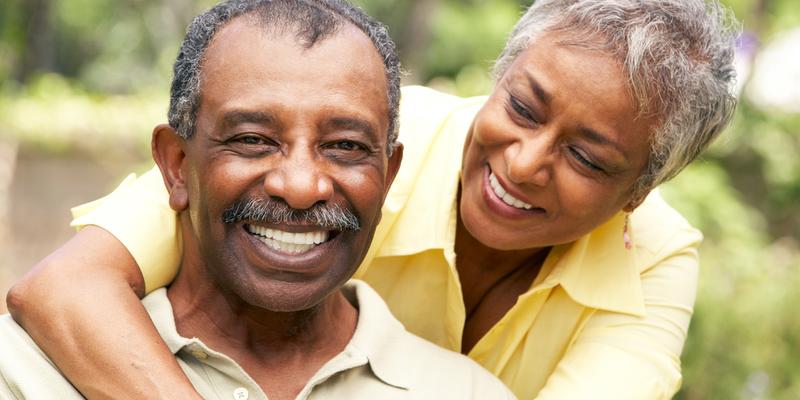 A senior african american woman hugs her husband in an outdoor setting.