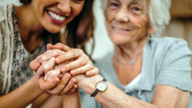 Close up photo of a young woman holding an older woman's hand.