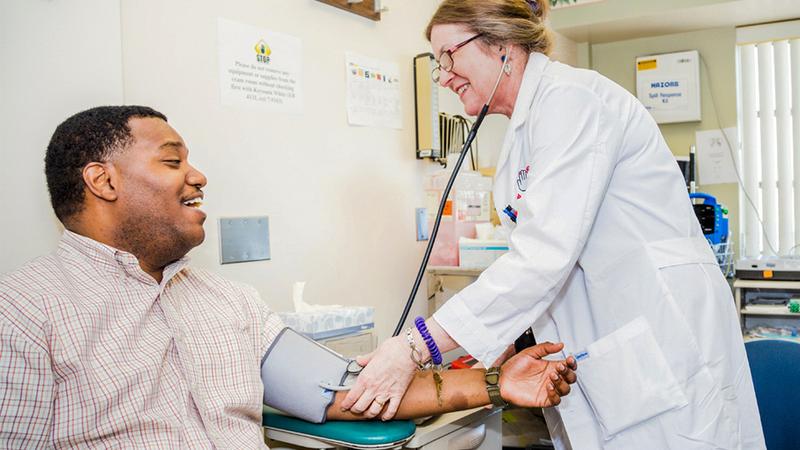 Dr. Michelle Magee takes the blood pressure reading for a male patient in a clinical setting.