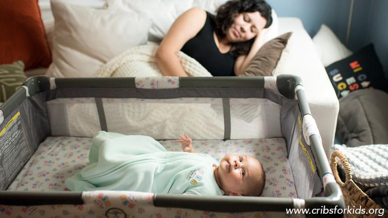 A mother takes a nap on a sofa while her newborn lays in a crib nearby.