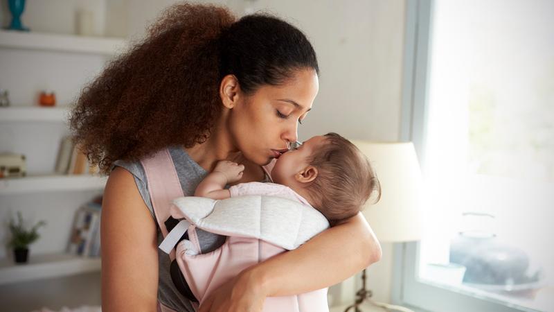 A mother holds her newborn baby and kisses it on the cheek.