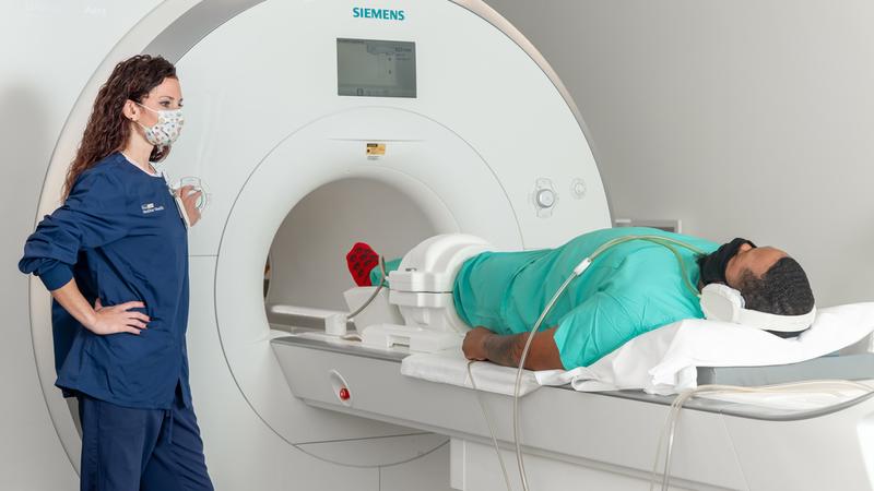 A radiology technician talks to a patient undergoing an MRI scan at MedStar Health. Both people are wearing masks.