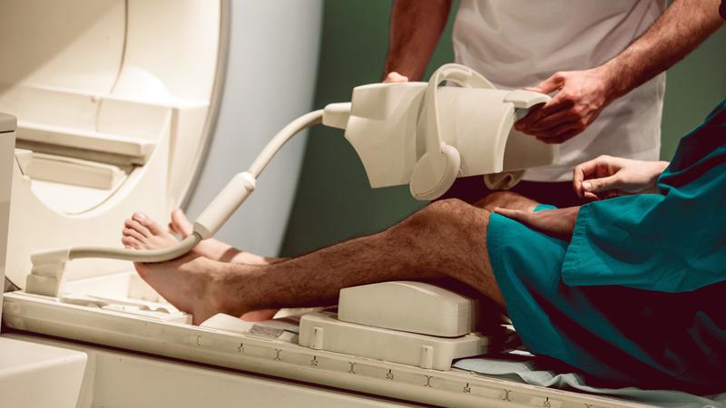 A radiology technician prepares a patient for an MRI scan of his knee.