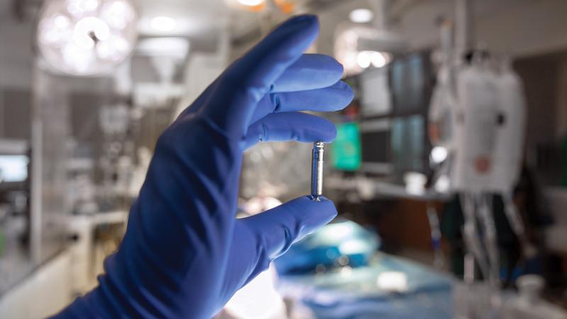 A close up photo of a gloved hand holding a leadless pacemaker device in a clinical setting.