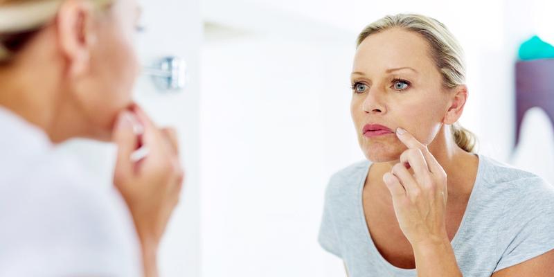 A woman looks in a mirror and touches her upper lip. 