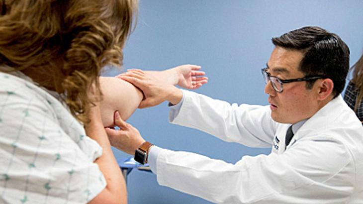 Dr David Song looks at a patient's arm during an office visit.