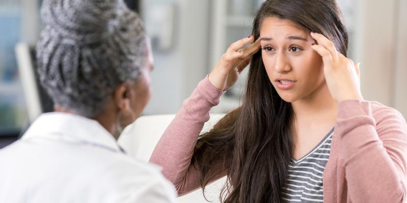 A young patient talks with a doctor about headache pain.