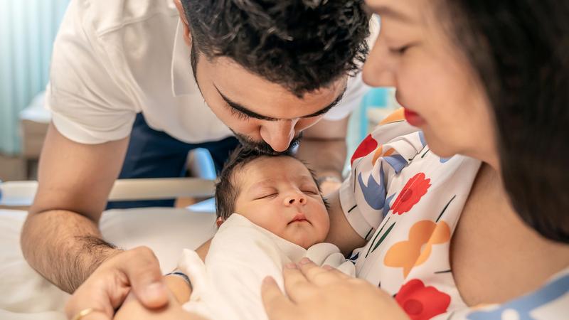 A mother holds her newborn baby while the father kisses the baby's forehead.