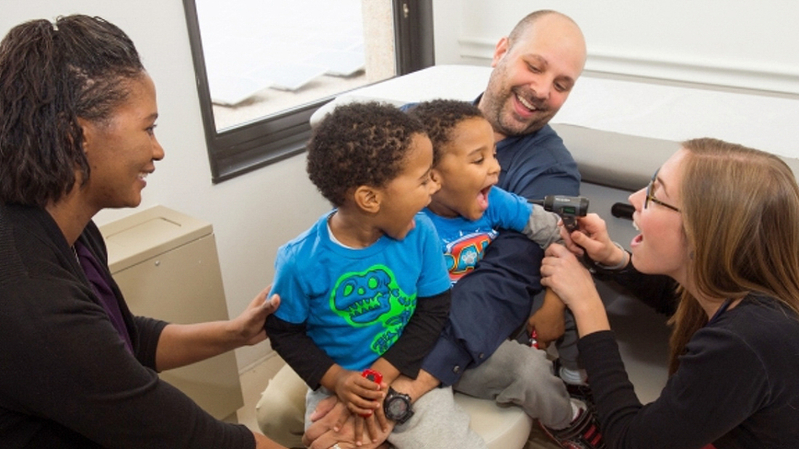 A doctor examines the throat of a pediatric patient during an office visit.
