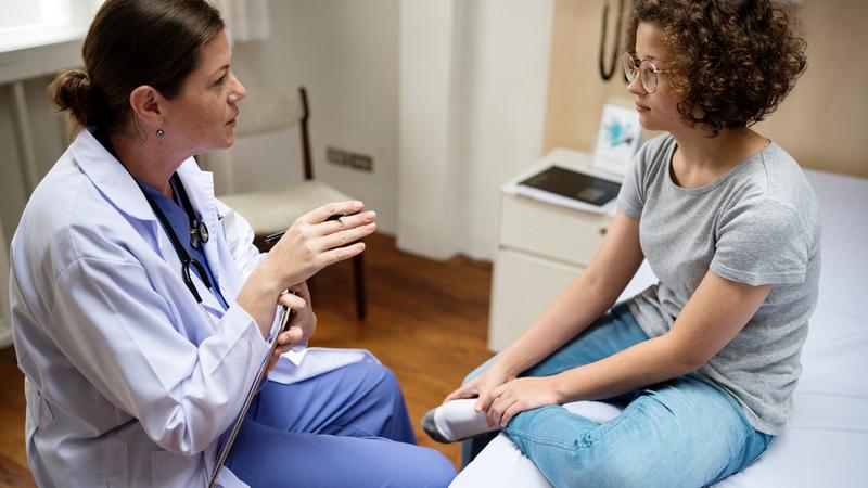 A doctor talks with an adolescent female patient in a clinical setting.