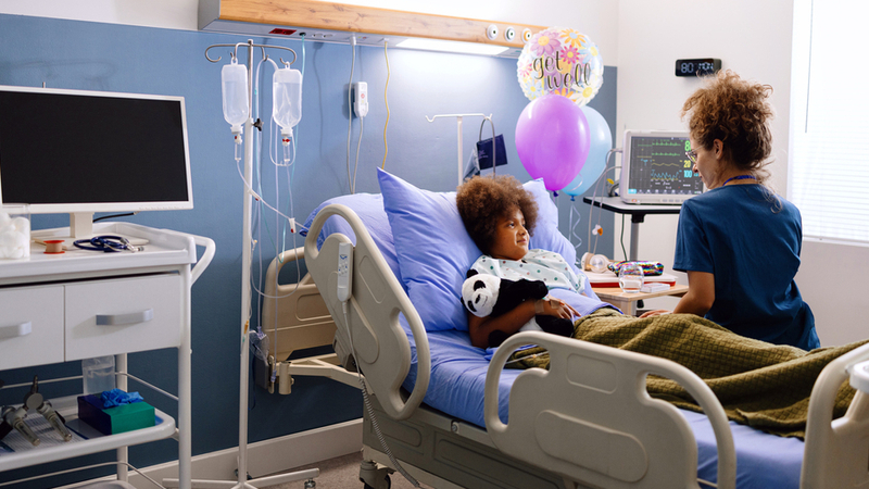 A nurse comforts a pediatric patient in a hospital room setting.