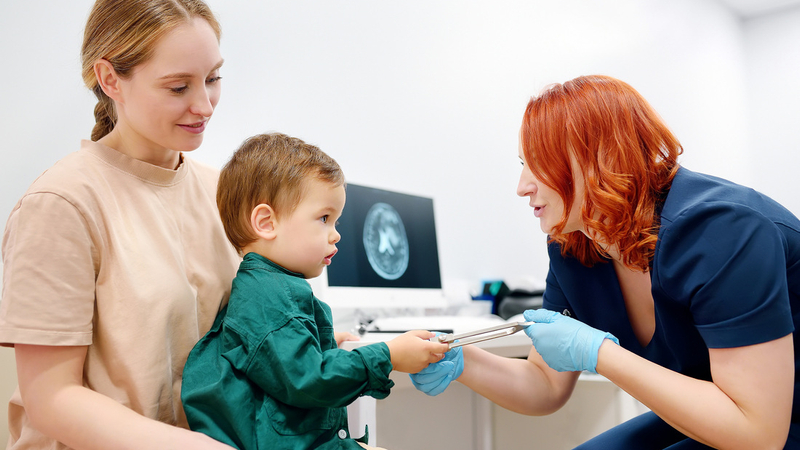 A healthcare professional talks with a young child and his mother during an office visit.