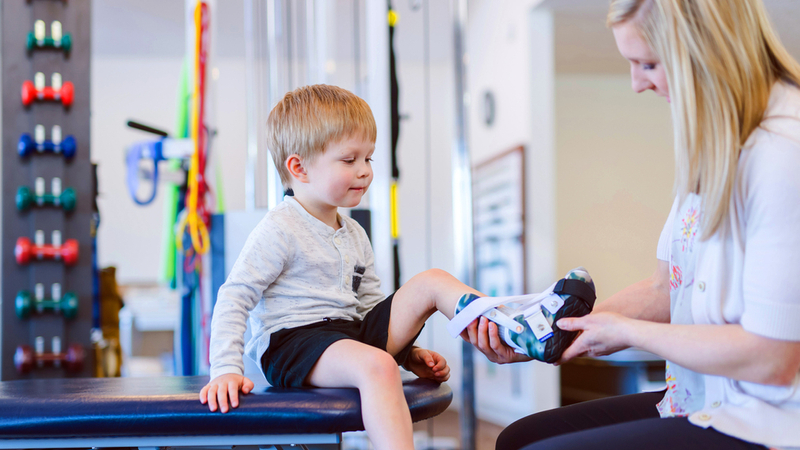 A young boy is fitted with a leg brace at a clininician's office.