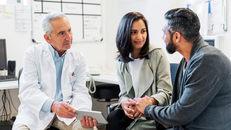 A couple talks with a doctor in a clinical setting.