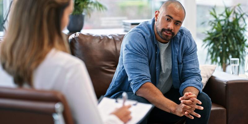 A man sits on a sofa and talks to a doctor wearing a white lab coat.