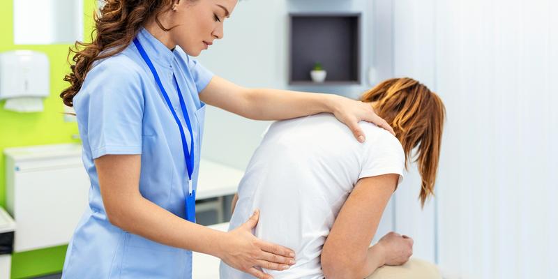 A doctor places hands on a patient to examine their spine during an office visit.