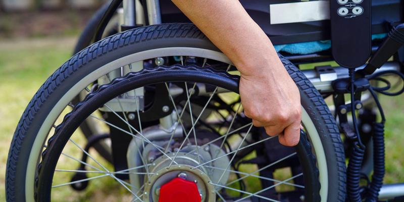 Close up photo of a hand on the wheel of a wheelchair.