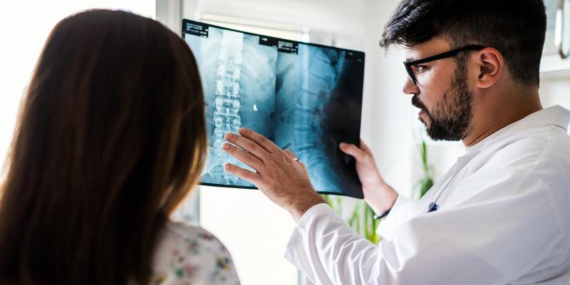 A doctor talks to a patient while holding an xray film of the spine.