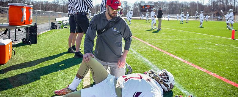 An athletic trainer works with a football player on the sidelines during a game.