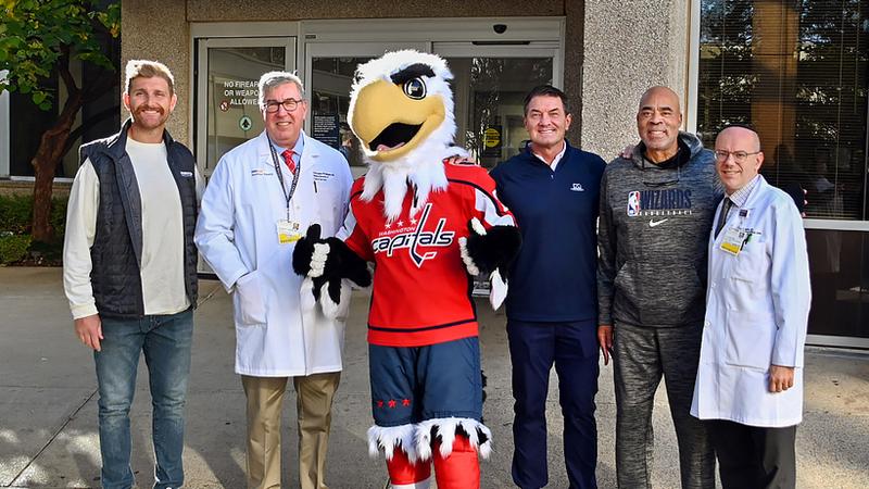 Sports medcine physicians pose for a photo outdoors with Washington DC's professional sports team representitives, including the Washington Capitals' mascot.