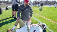 An athletic trainer works with a football player on the sidelines during a game.