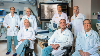 A team of MedStar cardiology doctors stand in a cardiac catheterization lab surrounded by modern technologic equipment.