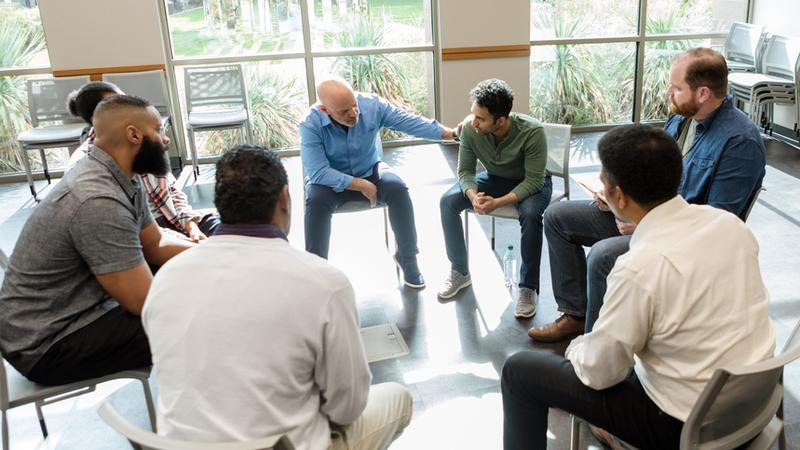 A group of men talk to each other during a group therapy support session.
